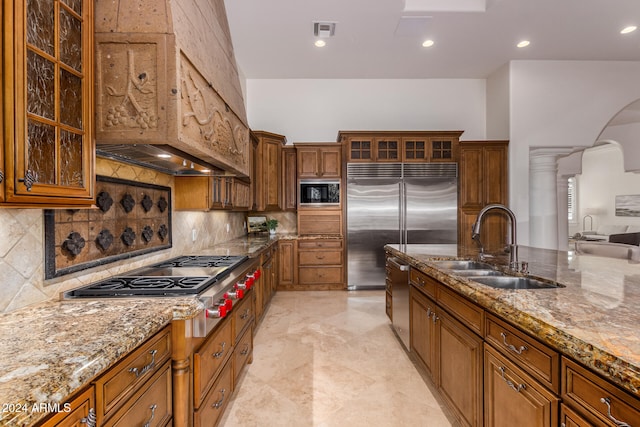 kitchen with built in appliances, sink, light stone counters, and ornate columns