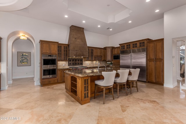 kitchen featuring premium range hood, a large island, built in appliances, decorative backsplash, and a high ceiling