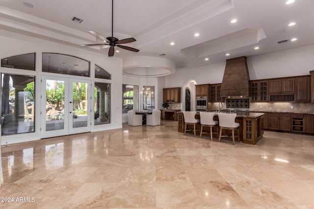 kitchen with a breakfast bar, a kitchen island with sink, stainless steel oven, premium range hood, and decorative backsplash