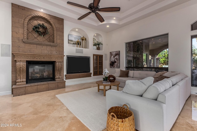 living room with a fireplace, ceiling fan, and a tray ceiling