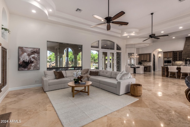 living room with a high ceiling, a raised ceiling, and ceiling fan with notable chandelier