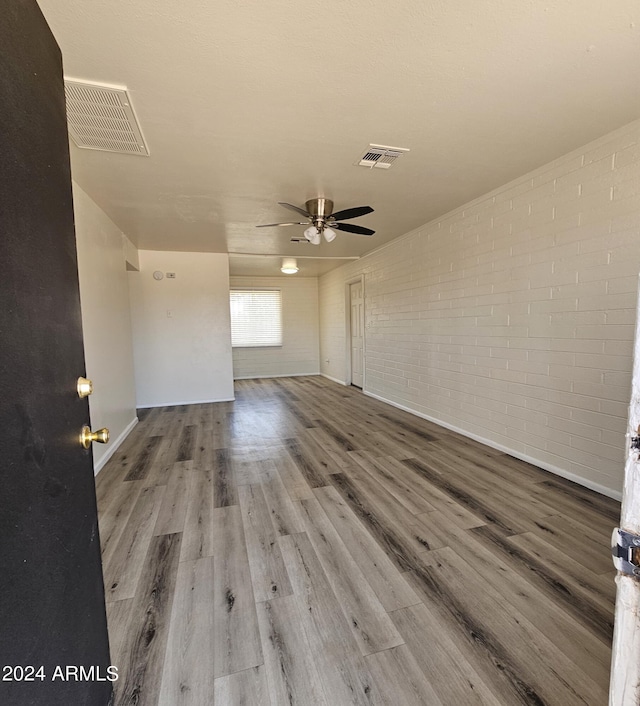 unfurnished living room with wood-type flooring, ceiling fan, and brick wall