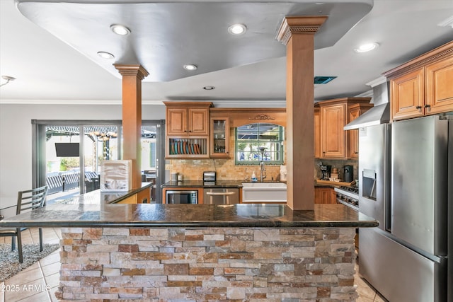 kitchen featuring appliances with stainless steel finishes, decorative columns, decorative backsplash, light tile patterned floors, and wall chimney exhaust hood