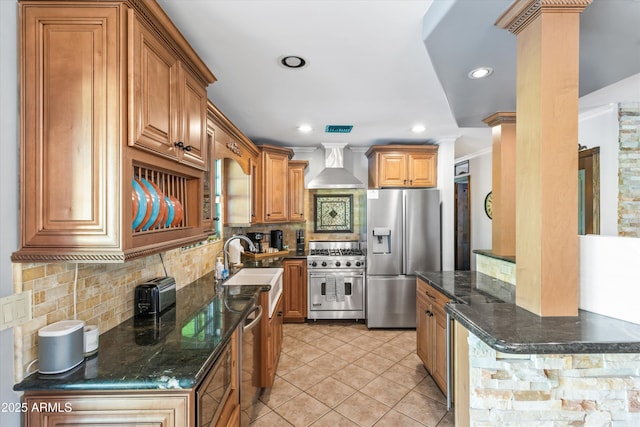 kitchen featuring ornate columns, sink, backsplash, stainless steel appliances, and wall chimney range hood