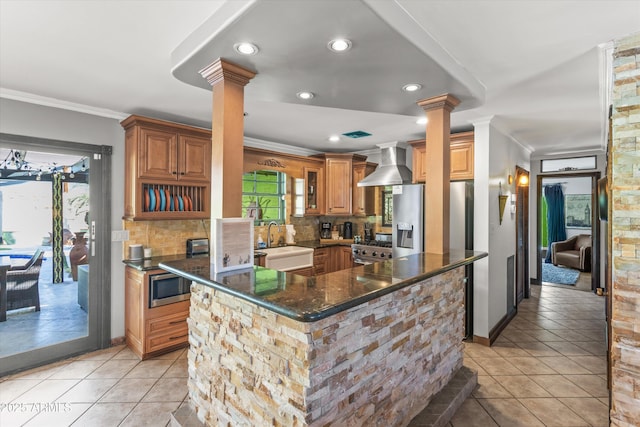 kitchen featuring decorative columns, appliances with stainless steel finishes, sink, and wall chimney range hood