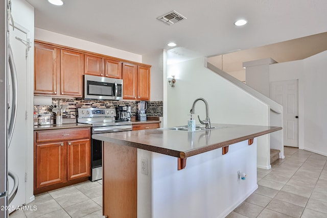 4318 W Apollo Rd, Laveen, AZ 85339 - kitchen with appliances with stainless steel finishes, light tile patterned floors, tasteful backsplash, an island with sink, and brown cabinetry