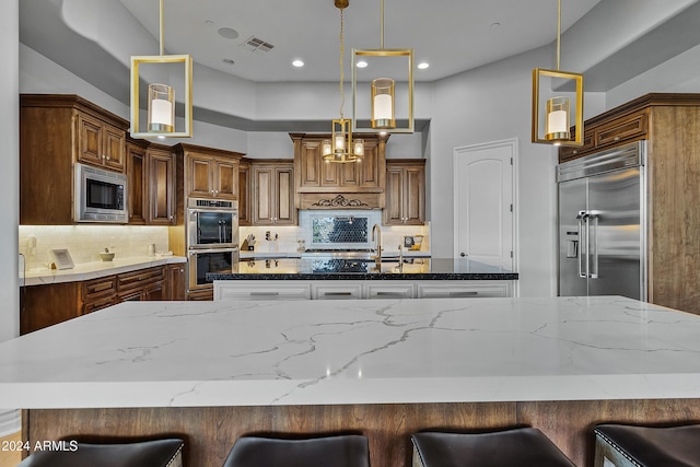 kitchen featuring a breakfast bar area, built in appliances, backsplash, and hanging light fixtures