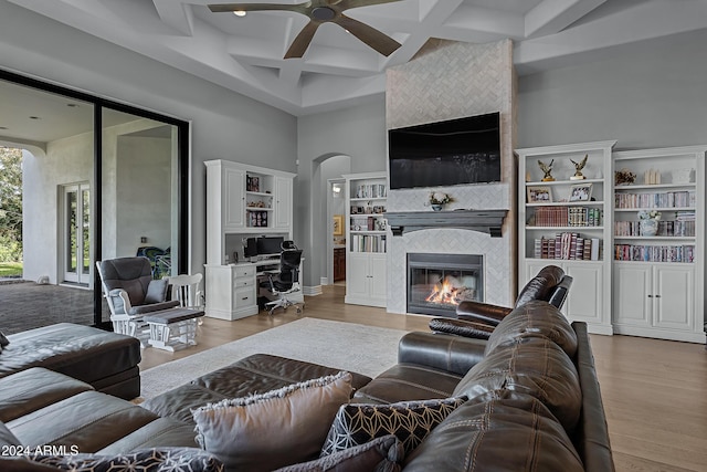 living room featuring coffered ceiling, ceiling fan, light wood-type flooring, beam ceiling, and a tiled fireplace