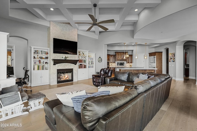 living room featuring built in shelves, ceiling fan, a tile fireplace, and light hardwood / wood-style floors