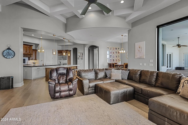 living room featuring coffered ceiling, ceiling fan with notable chandelier, sink, beam ceiling, and light hardwood / wood-style floors