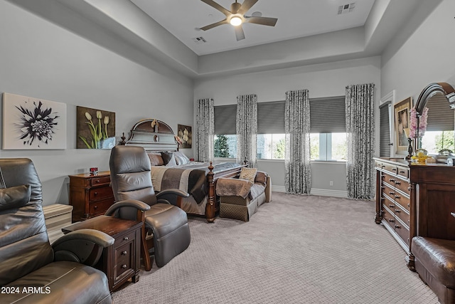 bedroom featuring a raised ceiling, ceiling fan, light colored carpet, and multiple windows