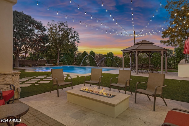 pool at dusk with a gazebo, pool water feature, a patio, and an outdoor fire pit