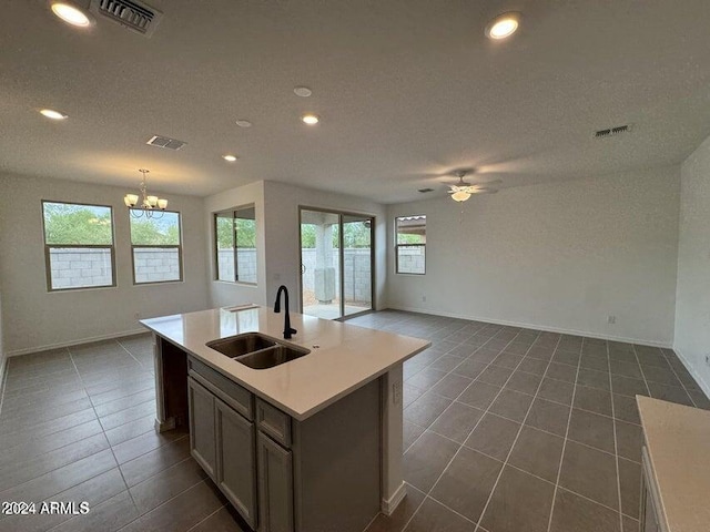 kitchen with a wealth of natural light, sink, ceiling fan with notable chandelier, and a center island with sink