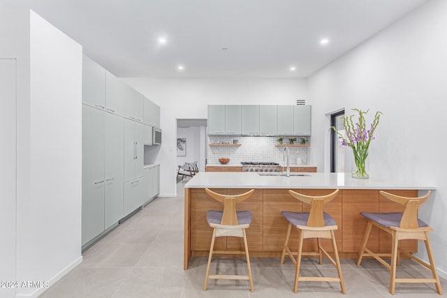 kitchen with sink, backsplash, gray cabinets, and a kitchen breakfast bar