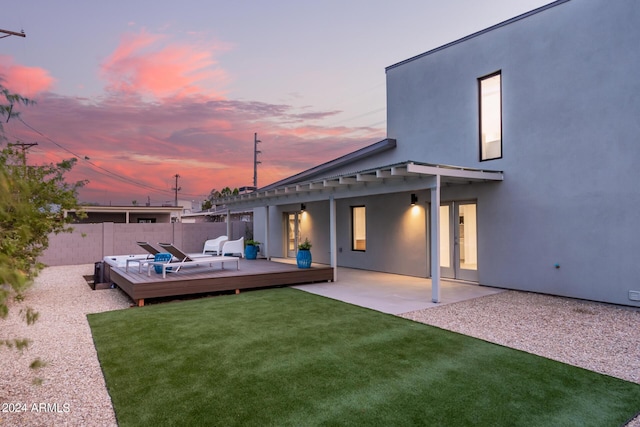 back house at dusk featuring a yard, a deck, and a patio area