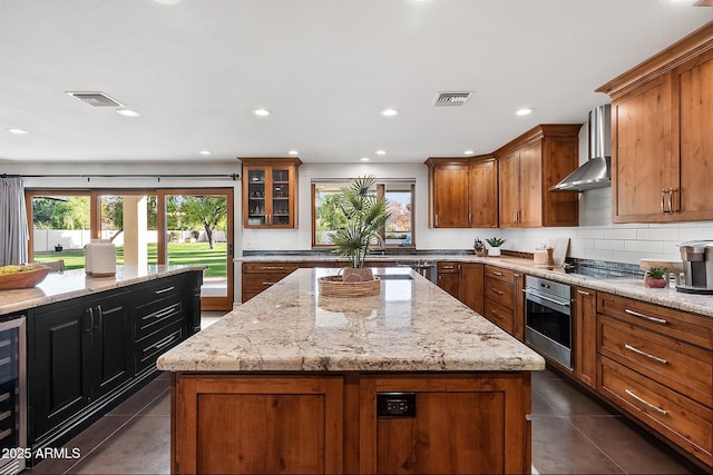 kitchen featuring light stone countertops, stainless steel appliances, wall chimney range hood, dark tile patterned flooring, and a center island