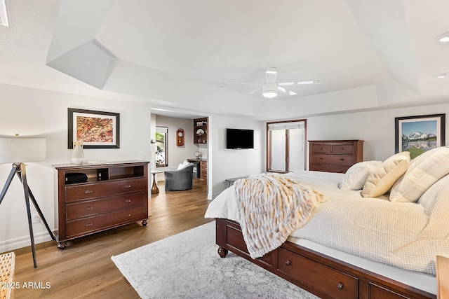 bedroom featuring ceiling fan, light hardwood / wood-style flooring, and a tray ceiling