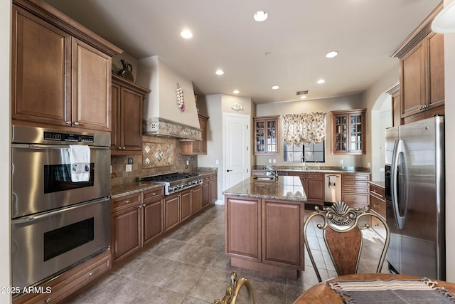 kitchen with sink, stone countertops, custom range hood, a kitchen island, and stainless steel appliances