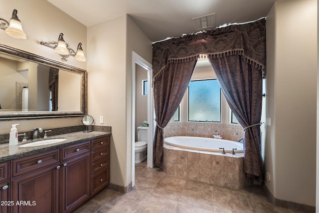 bathroom with vanity, toilet, and tiled bath