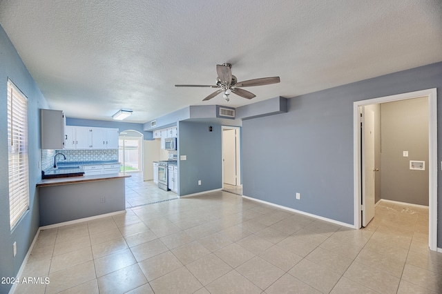 unfurnished living room with a textured ceiling, ceiling fan, light tile patterned floors, and sink