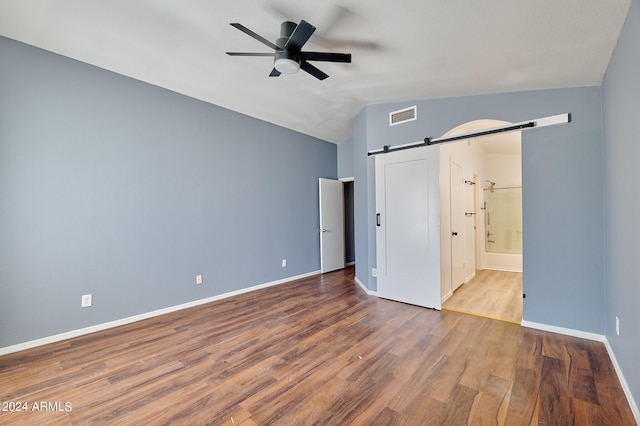 unfurnished bedroom with a barn door, hardwood / wood-style floors, ensuite bath, and ceiling fan