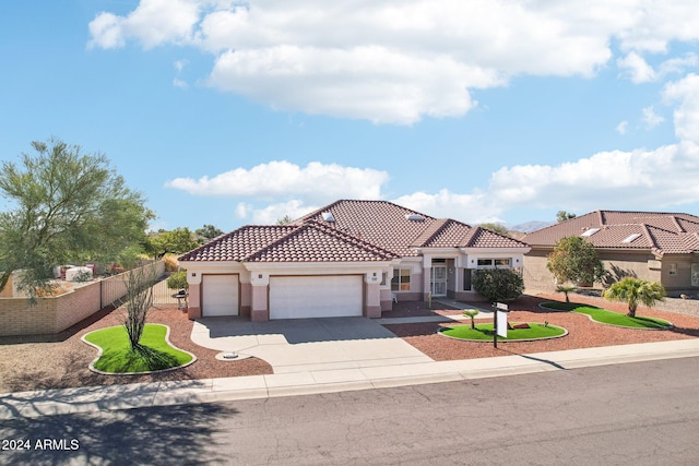 mediterranean / spanish house featuring a garage, driveway, a tiled roof, fence, and stucco siding