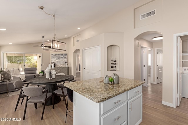 kitchen featuring ceiling fan with notable chandelier, a kitchen island, white cabinetry, hanging light fixtures, and vaulted ceiling