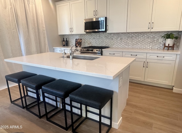 kitchen featuring white cabinets, stainless steel appliances, sink, and a center island with sink