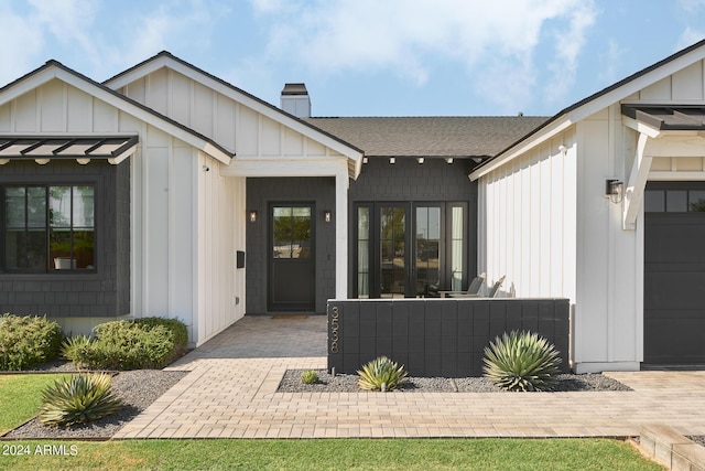 entrance to property featuring roof with shingles, a chimney, board and batten siding, a standing seam roof, and a garage