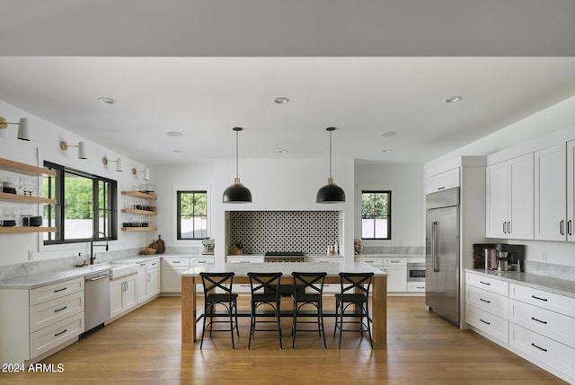 kitchen featuring a breakfast bar, stainless steel appliances, light wood-type flooring, open shelves, and a sink