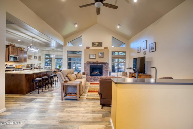 living room featuring high vaulted ceiling, sink, ceiling fan, a fireplace, and light hardwood / wood-style floors