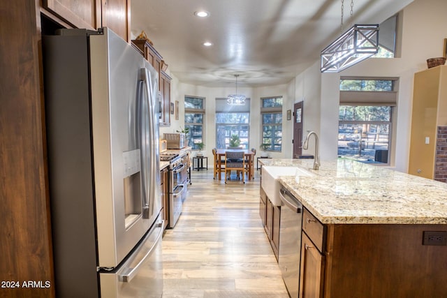 kitchen featuring light stone countertops, sink, hanging light fixtures, an island with sink, and appliances with stainless steel finishes