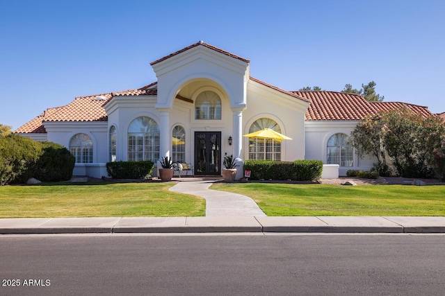 mediterranean / spanish home featuring a tiled roof, a front lawn, and stucco siding