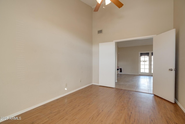 empty room with ceiling fan, a towering ceiling, and light hardwood / wood-style floors