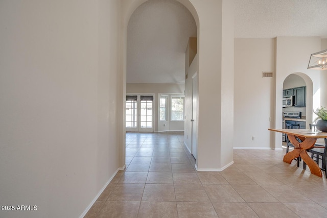 hall with a high ceiling, light tile patterned floors, and a textured ceiling