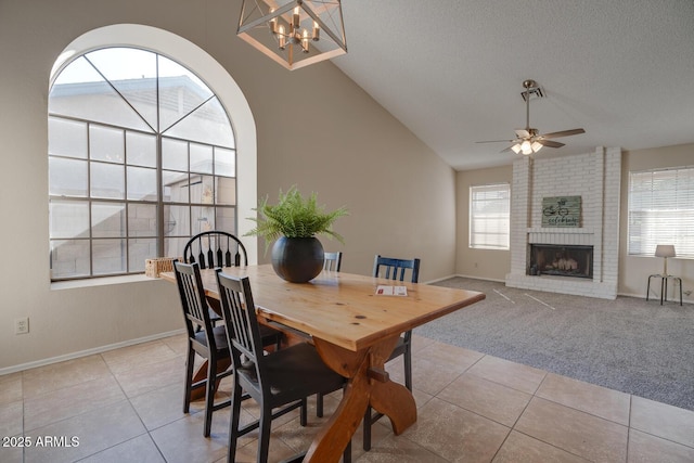 tiled dining room featuring lofted ceiling, a brick fireplace, ceiling fan with notable chandelier, and a textured ceiling