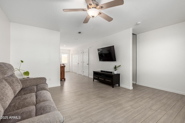 living area featuring light wood finished floors, a ceiling fan, visible vents, and baseboards