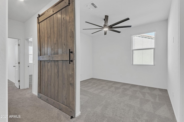 empty room with ceiling fan, a barn door, and light colored carpet