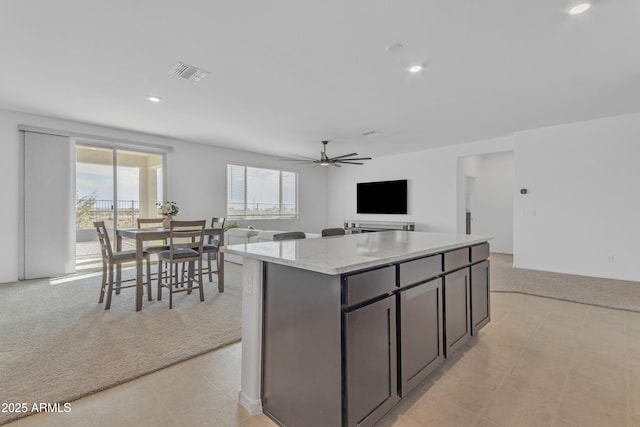 kitchen featuring a center island, light colored carpet, light stone counters, and ceiling fan