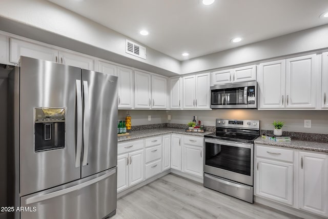 kitchen with light stone countertops, white cabinetry, appliances with stainless steel finishes, and light wood-type flooring