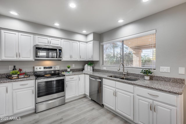 kitchen with stone countertops, sink, white cabinets, stainless steel appliances, and light wood-type flooring