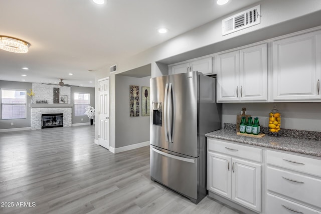 kitchen with a stone fireplace, white cabinetry, stainless steel fridge with ice dispenser, light wood-type flooring, and ceiling fan