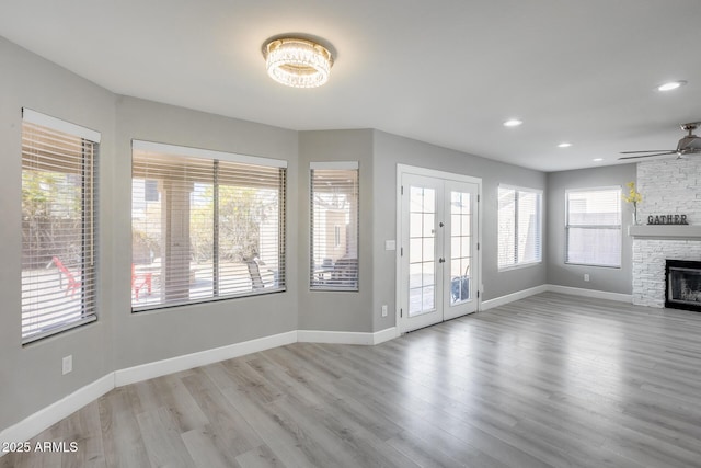 unfurnished living room featuring a stone fireplace, light hardwood / wood-style flooring, ceiling fan, and french doors