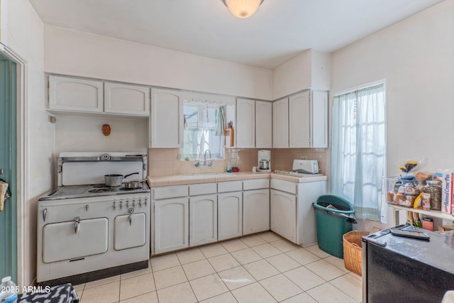 kitchen with white cabinetry, sink, backsplash, white range with gas stovetop, and light tile patterned floors