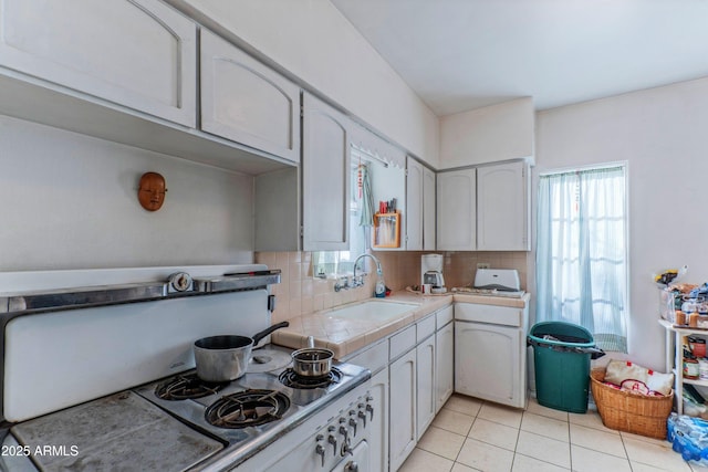 kitchen featuring light tile patterned floors, white cabinetry, backsplash, and sink