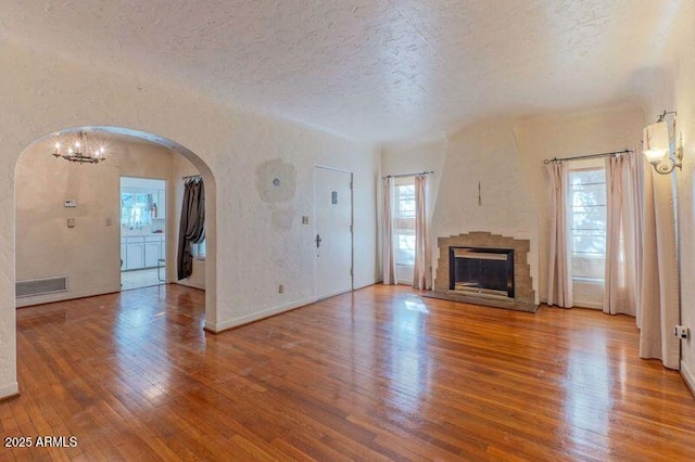 unfurnished living room with an inviting chandelier, a stone fireplace, a textured ceiling, and hardwood / wood-style flooring