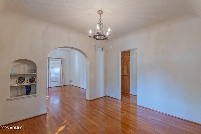 unfurnished room with hardwood / wood-style flooring, built in shelves, a textured ceiling, and a chandelier