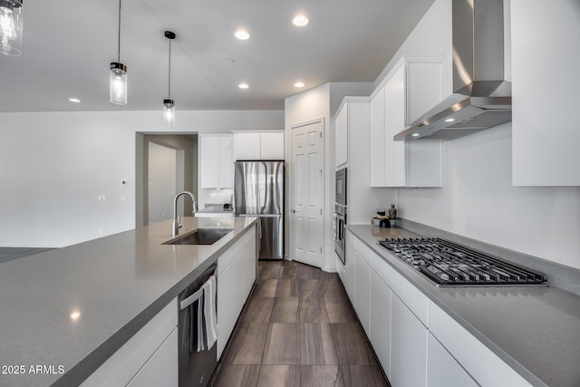 kitchen featuring a sink, decorative light fixtures, white cabinetry, stainless steel appliances, and wall chimney range hood