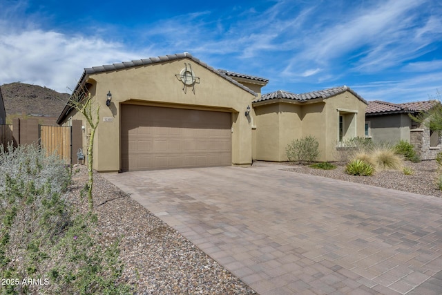 mediterranean / spanish-style home featuring stucco siding, a tile roof, decorative driveway, fence, and a garage