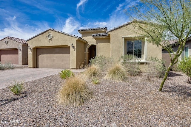 mediterranean / spanish-style house featuring stucco siding, a tiled roof, an attached garage, and driveway
